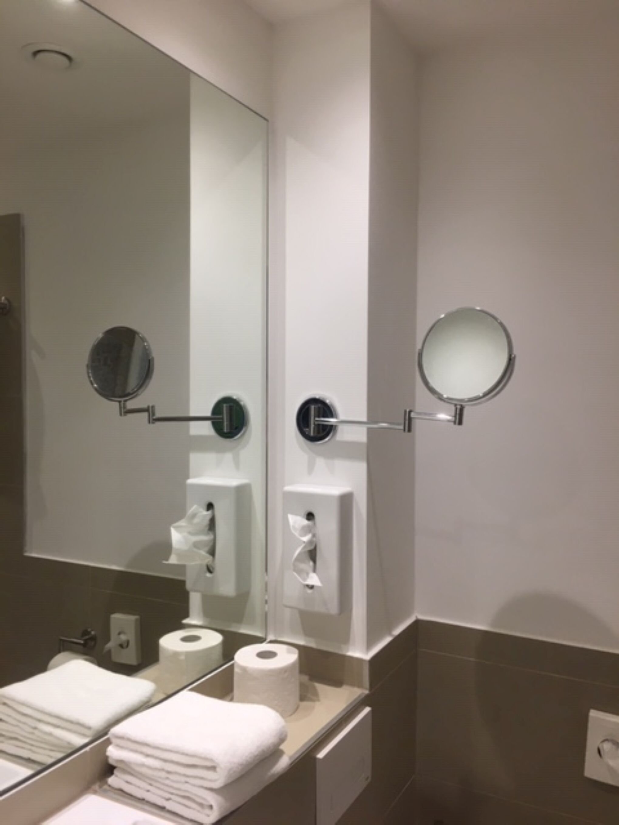 A modern bathroom with a large mirror, two round mirrors, a towel rack, and a toilet paper dispenser.