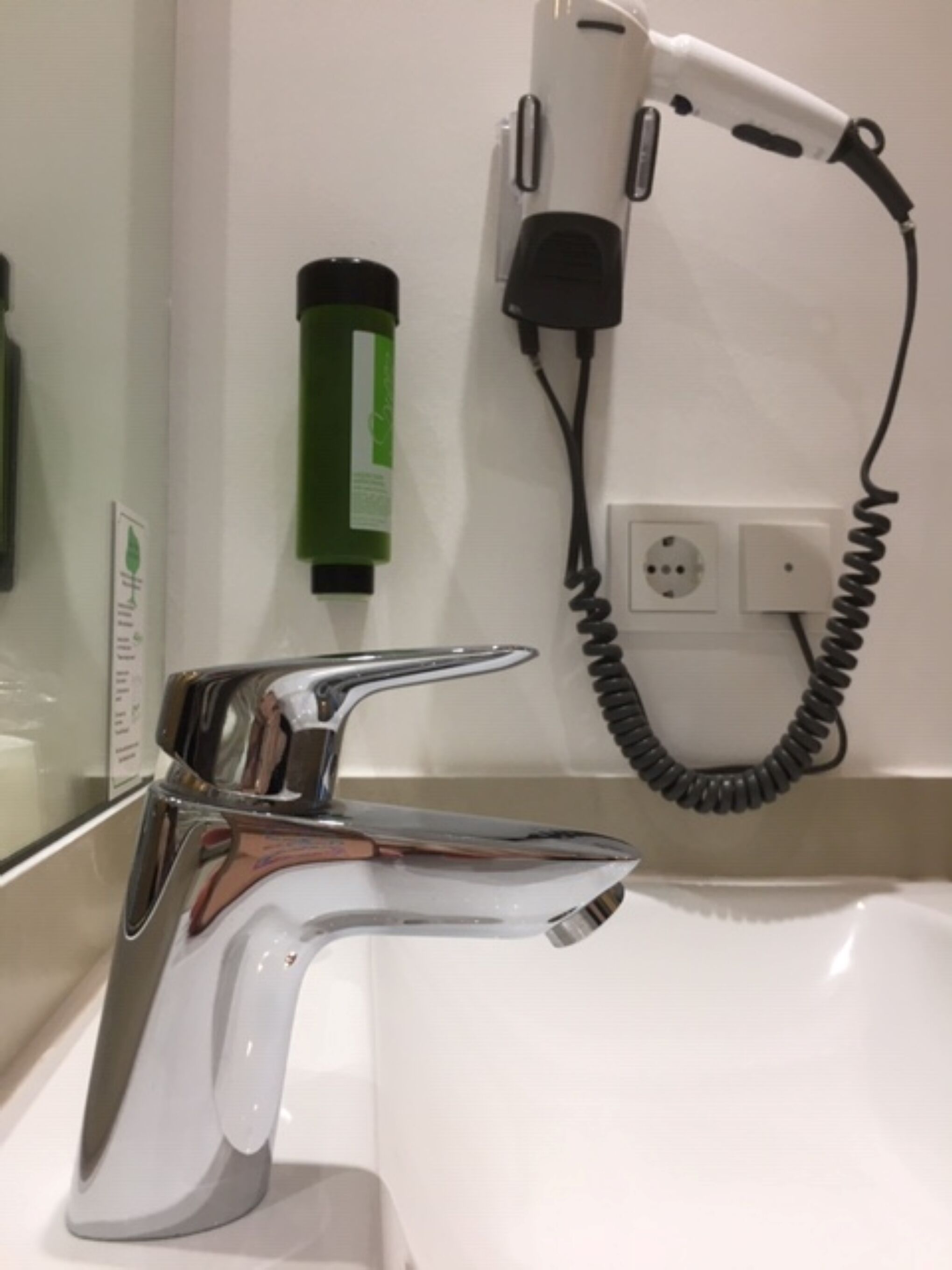 Un baño moderno con grifo cromado, secador de pelo y una botella verde de champú.