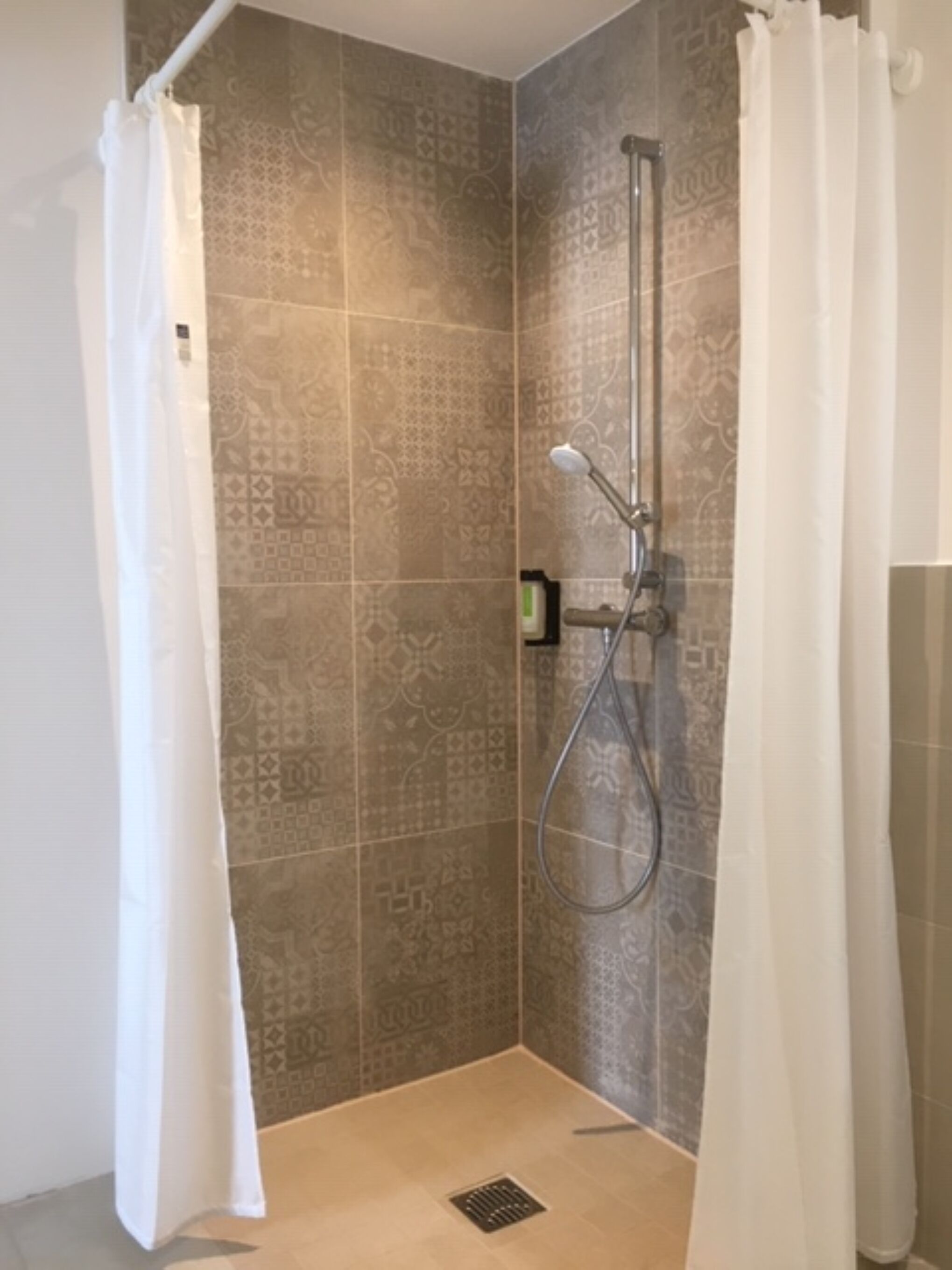 A shower area with patterned tiles, a handheld showerhead, and a floor drain.