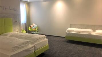 A hotel room with two beds, a green headboard, a small round table with a chair, and a wall with a simple line drawing.