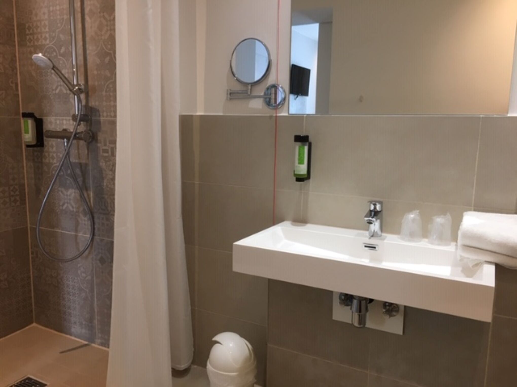 Een badkamer met een douche, wastafel, spiegel en handdoekhouder.