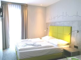A hotel room with a bed, a headboard, a wall with a city skyline design, and a window with curtains.
