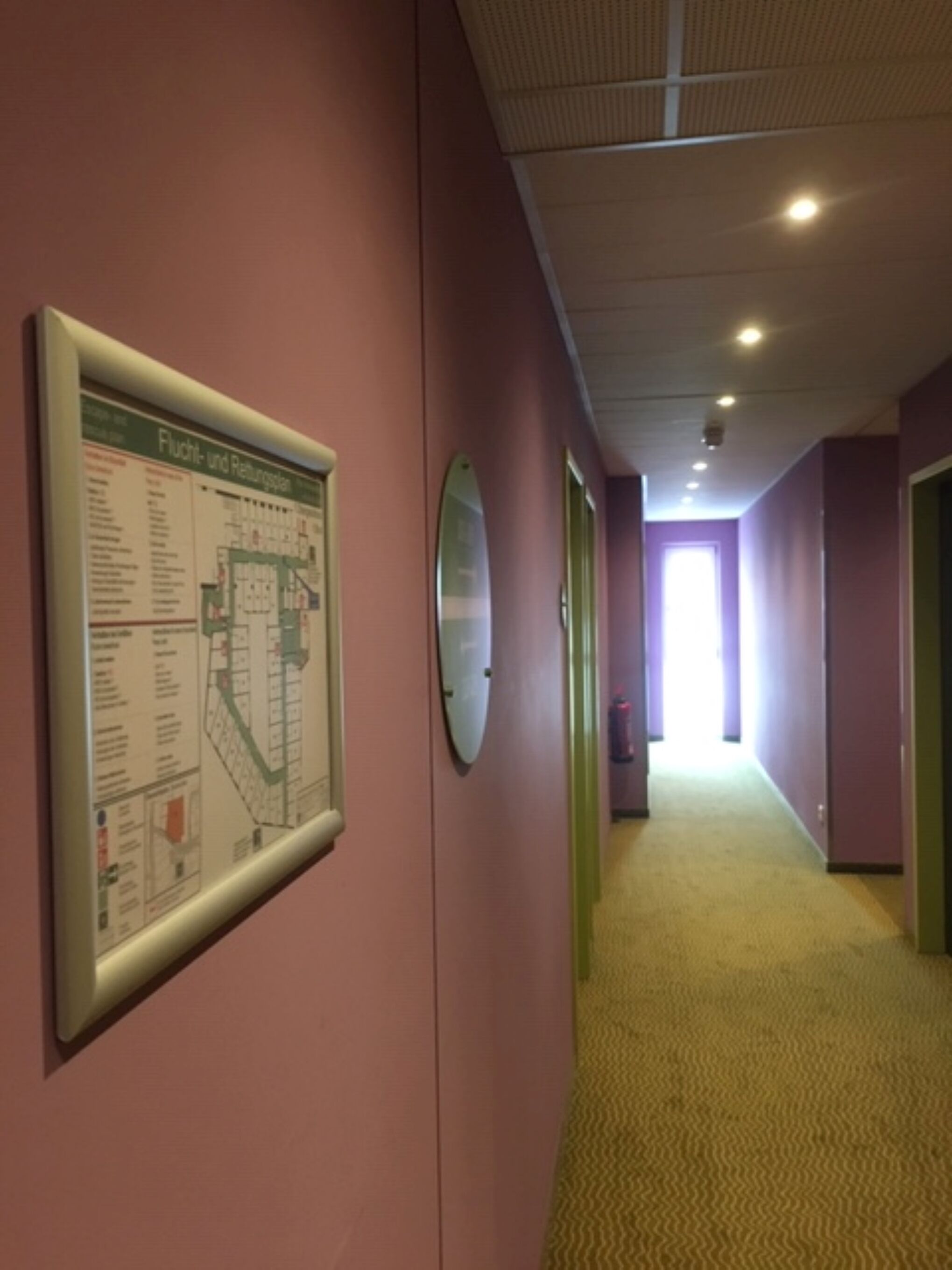 A corridor with pink walls, a yellow carpet, and a fire safety plan poster.