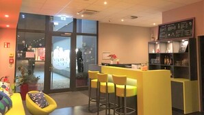 A modern bar area with yellow seating, a reception desk, and a menu board. - SleepySleepy Hotel Dillingen (Dillingen an der Donau)