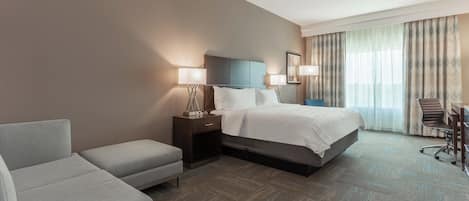 A hotel room with a bed, a desk, a chair, and a sofa.