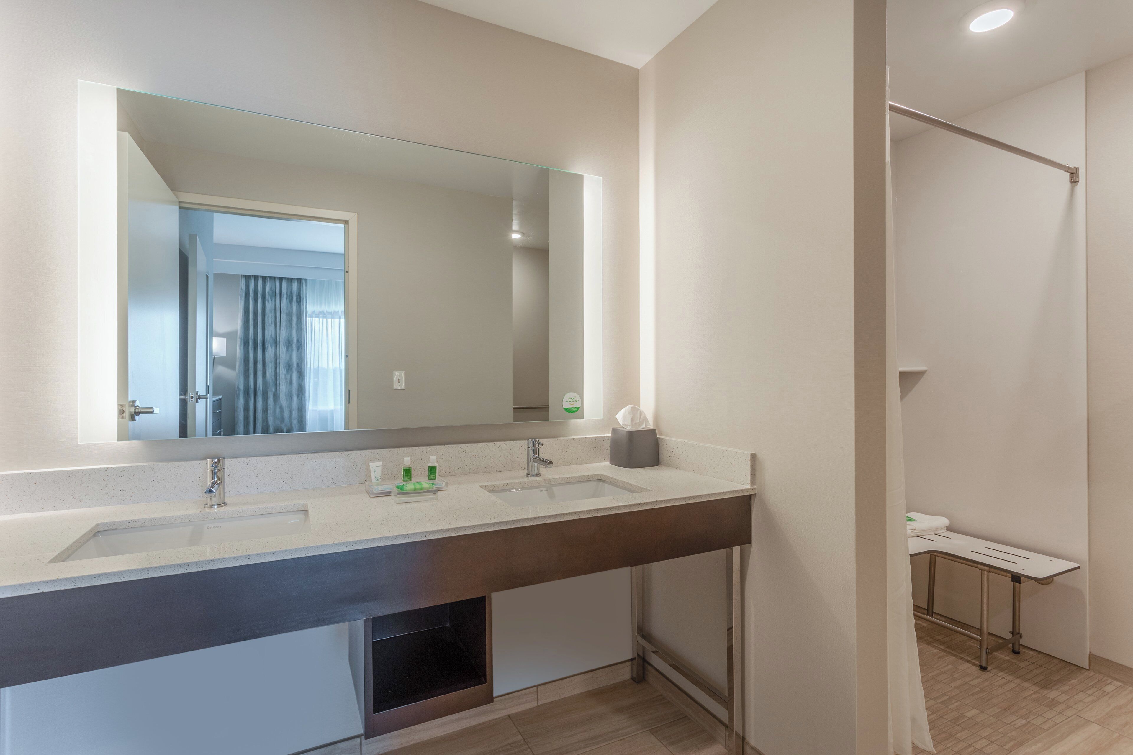 A modern bathroom with a large mirror, a double sink, and a shower area.