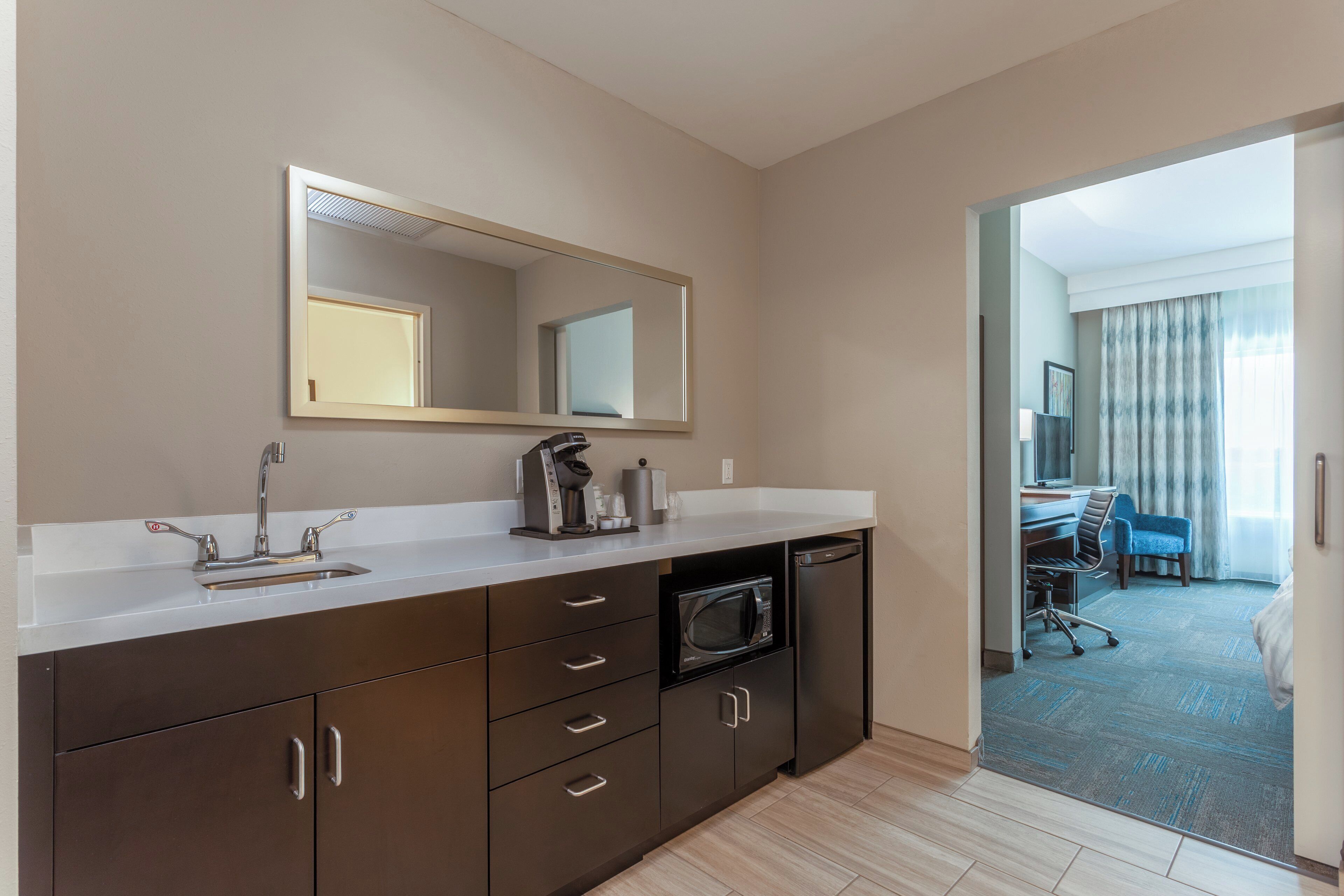 Une salle de bain d’hôtel équipée d’un grand miroir, d’un lavabo, d’une machine à café et d’un four à micro-ondes.