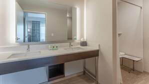 Een moderne badkamer met een grote spiegel, twee wastafels, een douchehoek en een klein tafeltje met toiletartikelen.