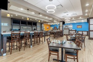 Un restaurante con varias mesas y sillas, una zona de bar con grifo de cerveza y una pared azul decorada con recuerdos deportivos.