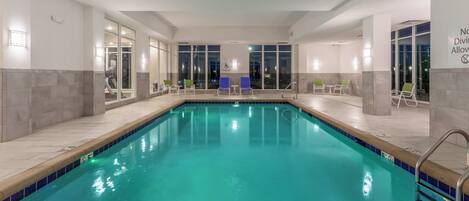 Una piscina con agua cristalina azul, rodeada de sillas de descanso y un elevador para piscina.