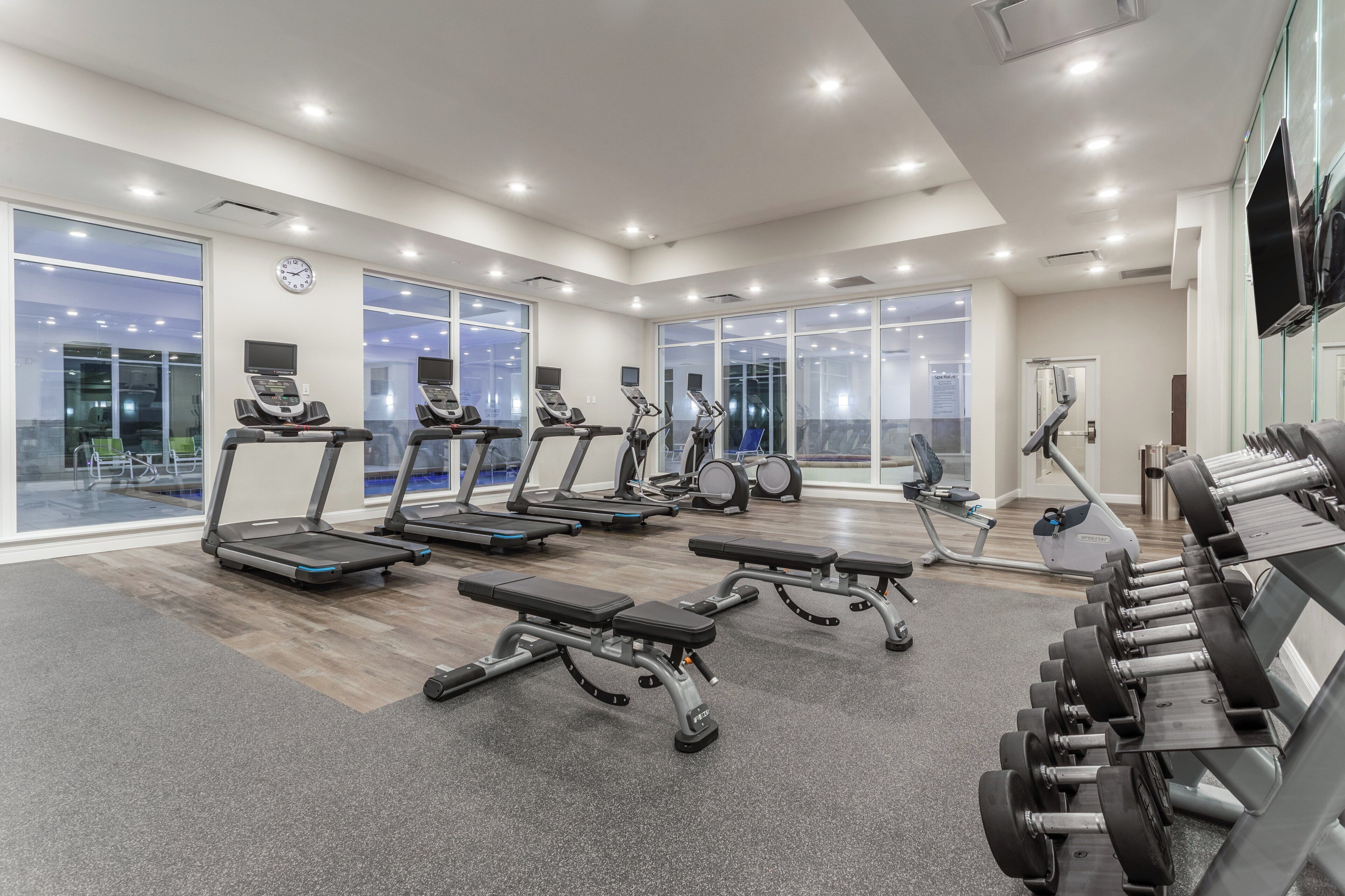 A modern gym with treadmills, benches, and dumbbells.