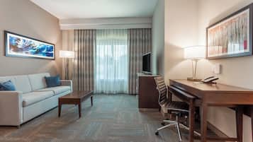 A hotel room with a sofa, a desk, a chair, a television, and a large window with curtains.
