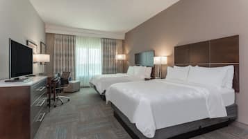A hotel room with two beds, a desk, a television, and a chair.