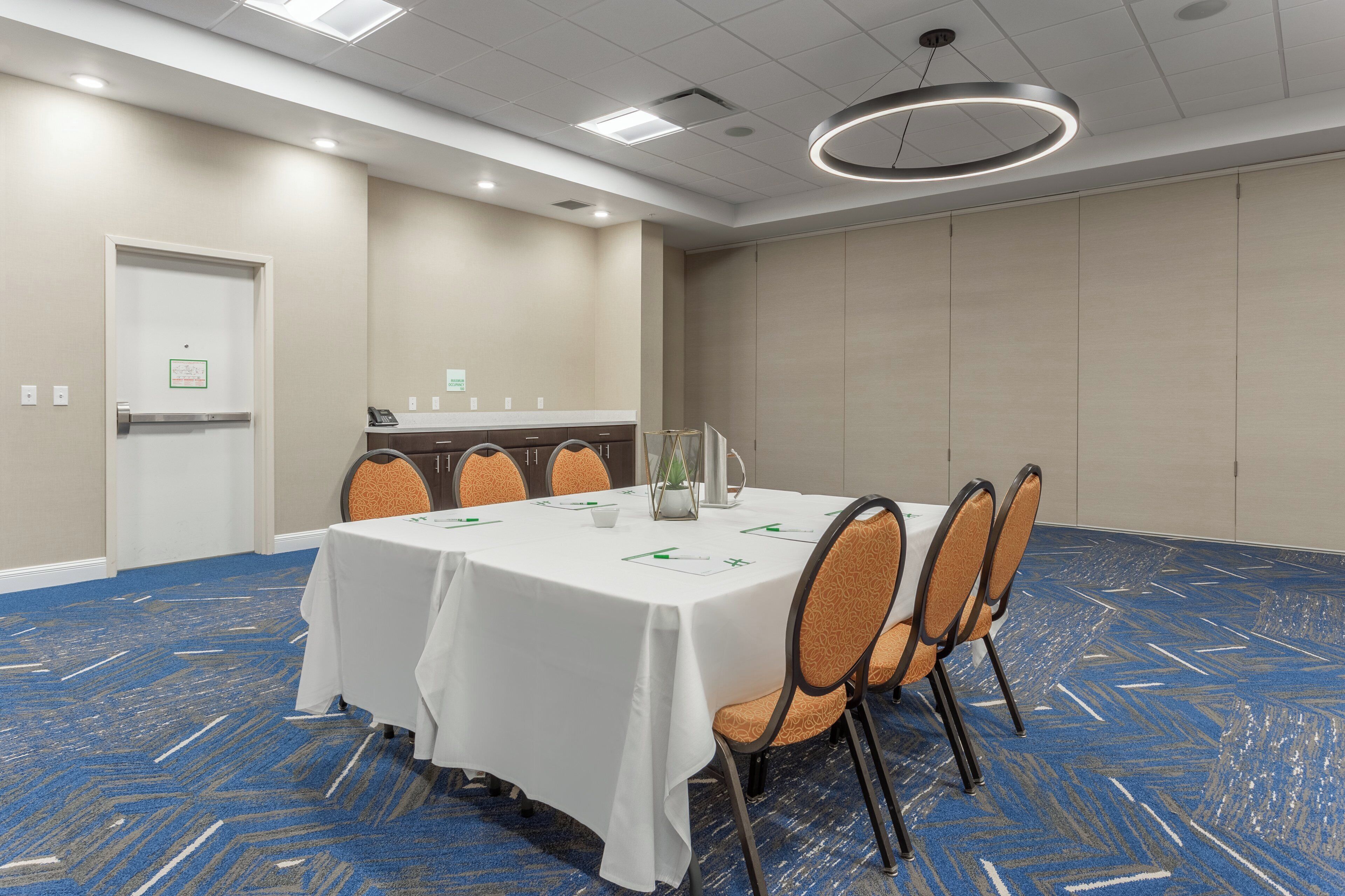 Un salón de conferencias con una mesa blanca, sillas anaranjadas y una alfombra azul.
