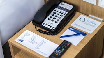 Un comptoir de réception d’hôtel avec un téléphone, une télécommande et quelques documents.