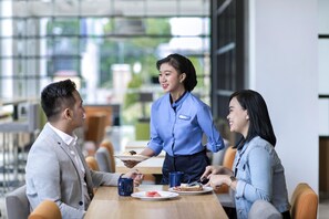 A waiter serving food to guests in a modern dining area with glass walls and natural light. - Holiday Inn Express Jakarta Menteng by IHG (Jakarta)