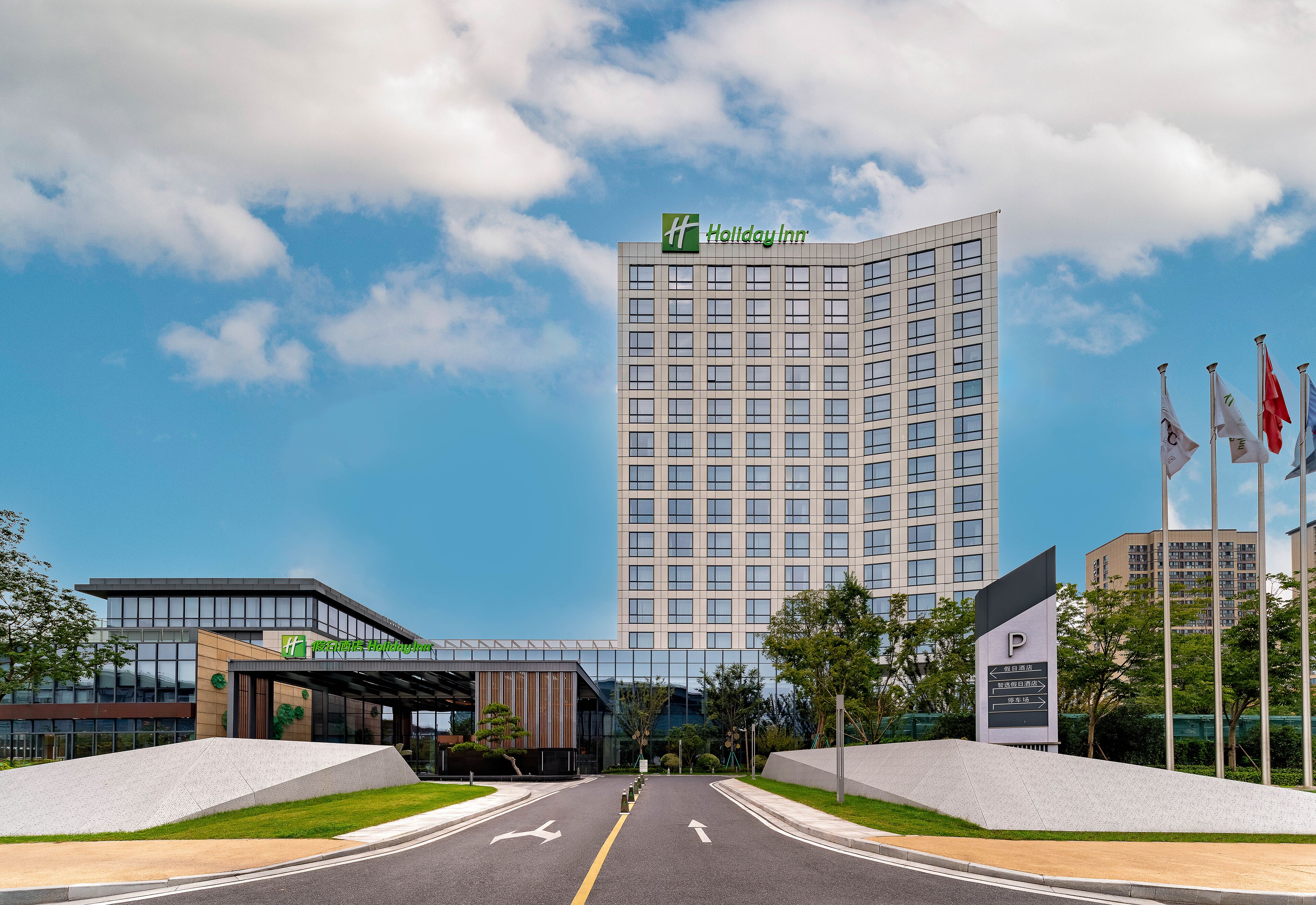 A modern Holiday Inn hotel with a prominent 'P' sign for parking, a clear sky, and a well-maintained entrance area.