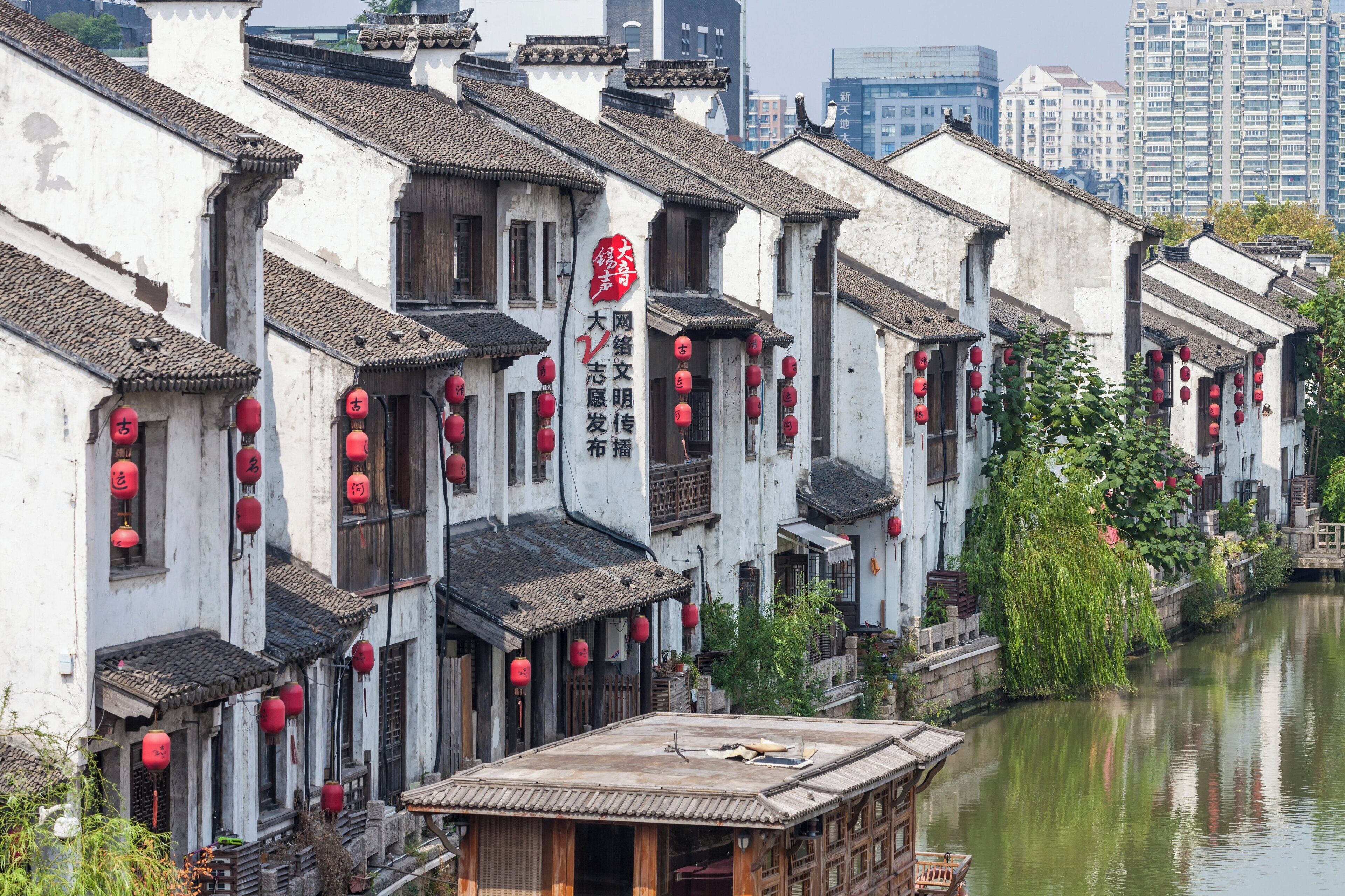 Traditionelle chinesische Architektur mit roten Laternen, ein Fluss und im Hintergrund moderne Gebäude.