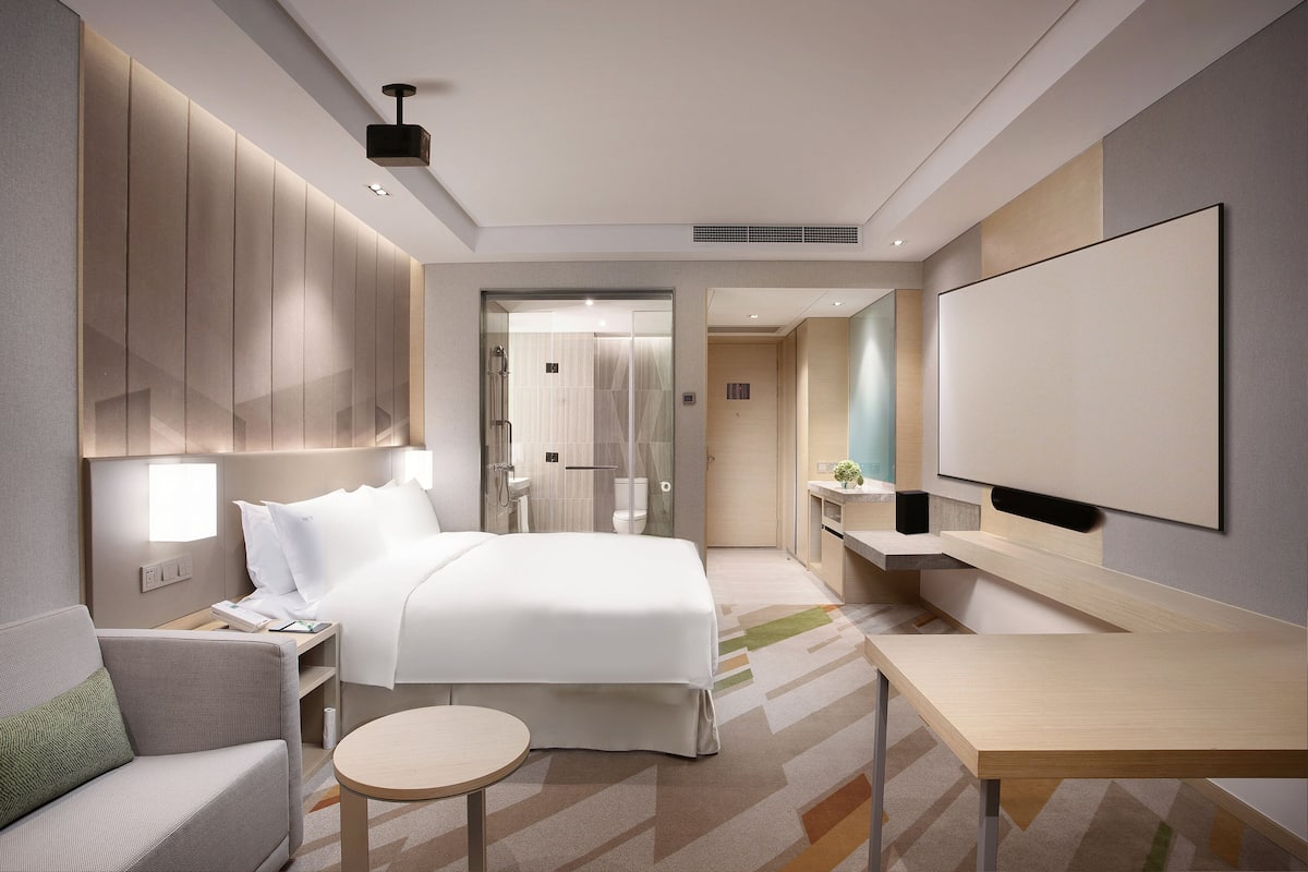 Ein modernes Hotelzimmer mit einem großen Bett, einer Couch, einem kleinen runden Tisch und einem an der Wand befestigten Fernseher.