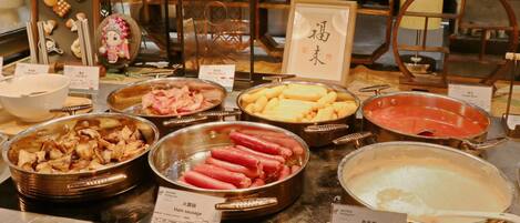 Buffet com diversos pratos, incluindo presunto, linguiça, feijão cozido e uma grande panela de aveia.