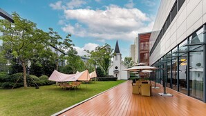 Eine Terrasse im Freien mit Holzboden, Sitzgelegenheiten und Blick auf eine Kirche.