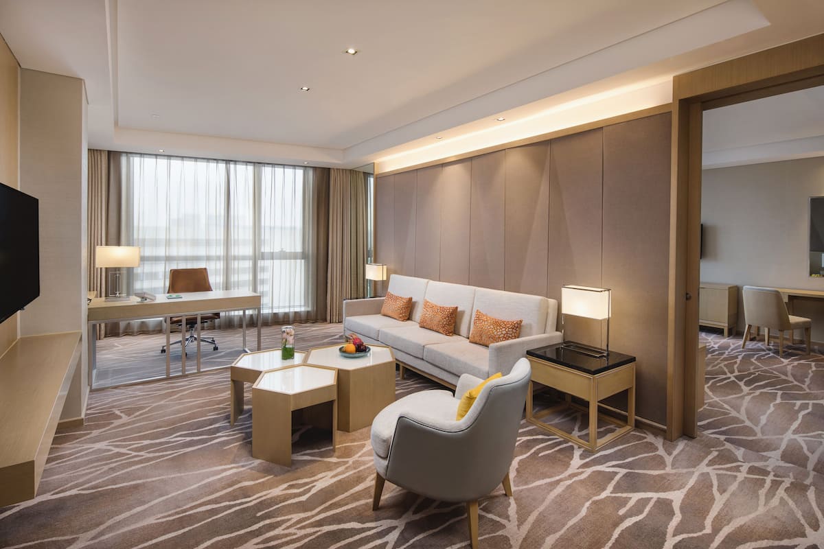 Ein modernes Hotelzimmer mit einer Couch, Sesseln, einem Schreibtisch und einem Flachbildfernseher.