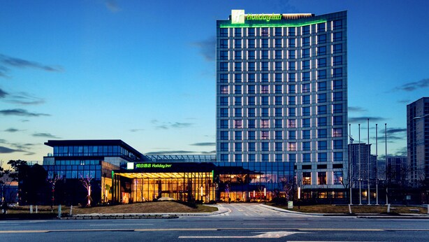 Ein modernes Hotel mit Glasfassade, einem Holiday Inn-Schild und einem markanten grünen Schild oben.
