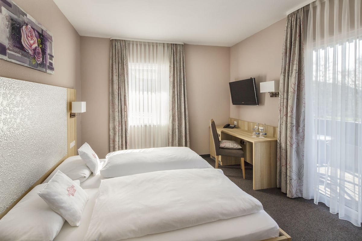 Een hotelkamer met twee bedden, een bureau, een stoel, een televisie en een raam met gordijnen.