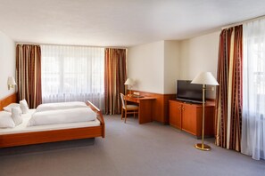 A hotel room with a bed, desk, TV, and curtains.