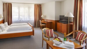 Een hotelkamer met een bed, een bureau met een televisie, een stoel, een tafel met een fles champagne en gordijnen.