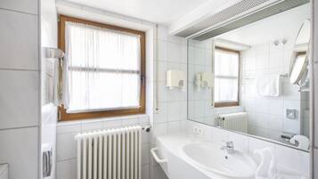 Un baño moderno con un lavamanos blanco, un espejo grande, una ventana con cortina blanca y un radiador blanco.