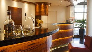 Een bargedeelte met een gebogen houten toonbank, barkrukken en een fles Chivas Regal.