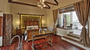 A room with a wooden floor, a stone wall, a bed with a wooden headboard, a table with a vase, and a window with curtains. - On Hotel Boutique (Sucre)