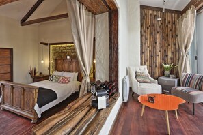 Quarto com cama de madeira, um sofá, uma mesa de centro e um espaço de estar com vista para uma parede de pedra.