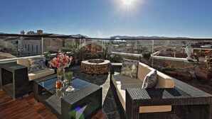 A rooftop terrace with wicker furniture, a glass table, and a view of a cityscape and mountains. - On Hotel Boutique (Sucre)