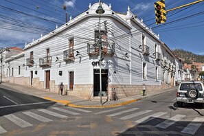 Um edifício histórico com fachada branca, entrada destacada e vista da rua com faixa de pedestres.
