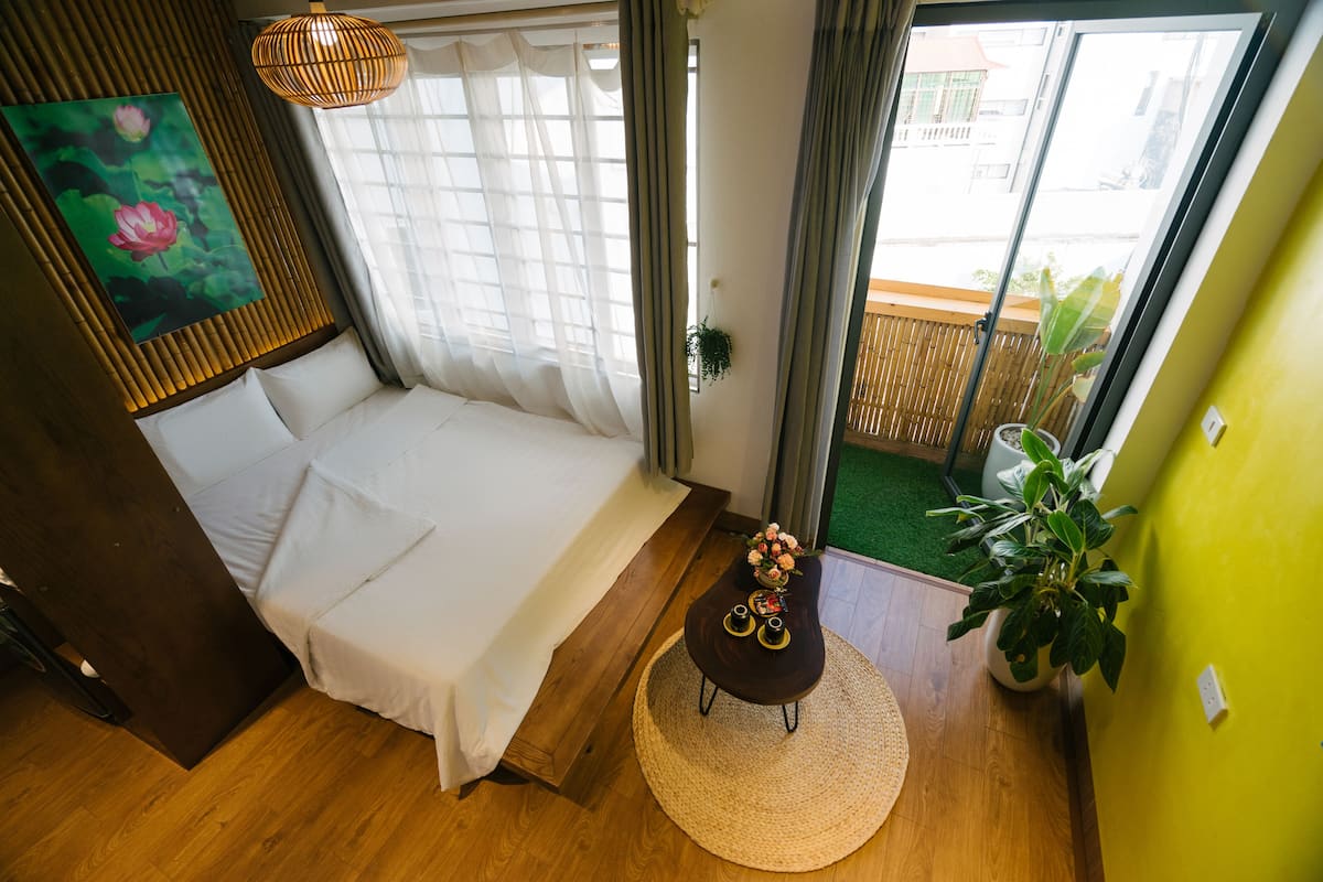 Un dormitorio con cama, una mesita de noche con un florero, una planta en maceta y vistas al balcón exterior.