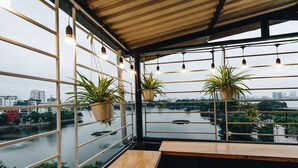 A room with a view of a river, potted plants, hanging lights, and wooden furniture. - The Autumn Homestay (Hanoi)