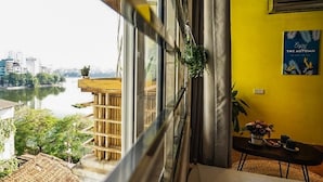 A room with a view of a river and cityscape, a wooden balcony, and a table with a plant. - The Autumn Homestay (Hanoi)