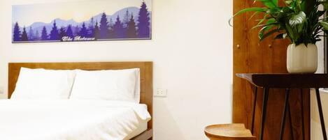Une chambre à coucher avec un lit, une tête de lit en bois, un tableau accroché au mur, une plante en pot et un petit tabouret en bois.