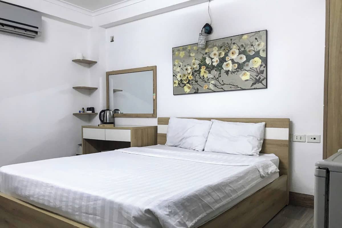 Habitación de hotel ordenada con cama, mesita de noche, espejo y un cuadro colgado en la pared.