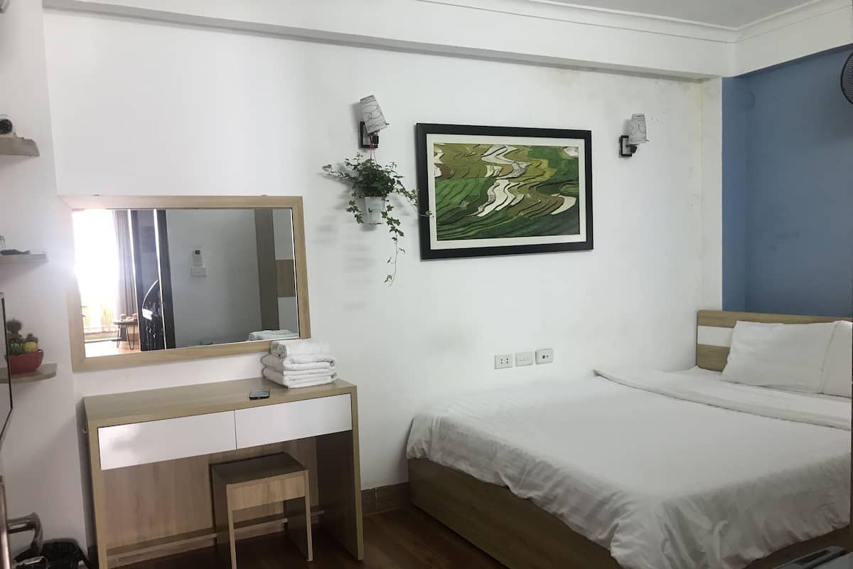 Un dormitorio con cama, mesita de noche, espejo, lámpara de pared y un cuadro enmarcado.