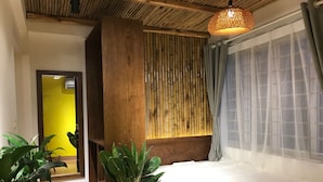 A bedroom with a bed, a potted plant, a bamboo wall, and a window with curtains. - The Autumn Homestay (Hanoi)