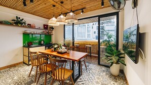A dining area with a wooden table and chairs, a green counter, and a large window offering a view of buildings outside. - The Autumn Homestay (Hanoi)