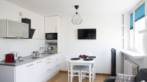 A modern kitchen with white cabinetry, a dining table with chairs, a flat-screen TV, and a unique geometric pendant light. - Plac Teatralny - Imaginea City Apartments (Warsaw)
