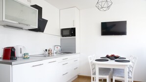A modern kitchen with white cabinetry, a microwave, a kettle, and a dining area with a white table and chairs. - Plac Teatralny - Imaginea City Apartments (Warsaw)
