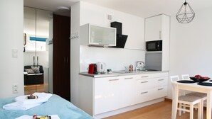 A modern hotel room with a kitchenette, a bed with blue bedding, a dining area with a table and chairs, and a mirror reflecting the room. - Plac Teatralny - Imaginea City Apartments (Warsaw)