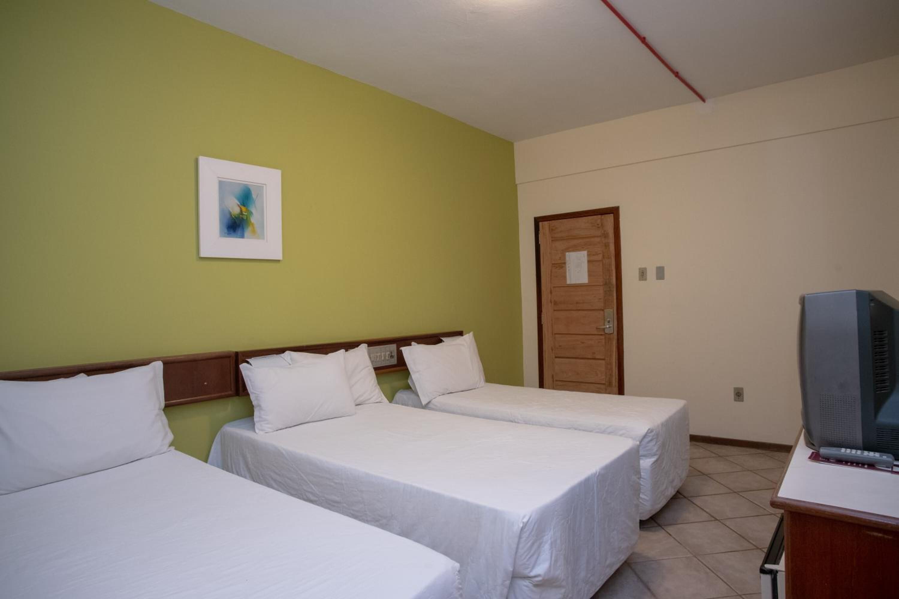 A hotel room with two single beds, a wooden door, a television on a desk, and a framed picture on the wall.
