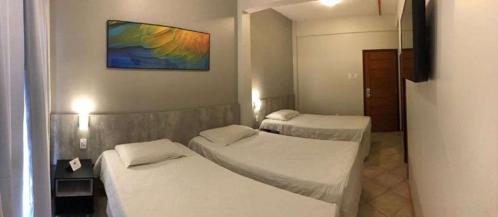 A hotel room with two beds, a painting on the wall, a bedside table, and a door.