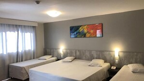 Una camera d'albergo con due letti singoli, un'ampia finestra con tende, un quadro astratto dai colori vivaci appeso alla parete e un comodino con un telefono.